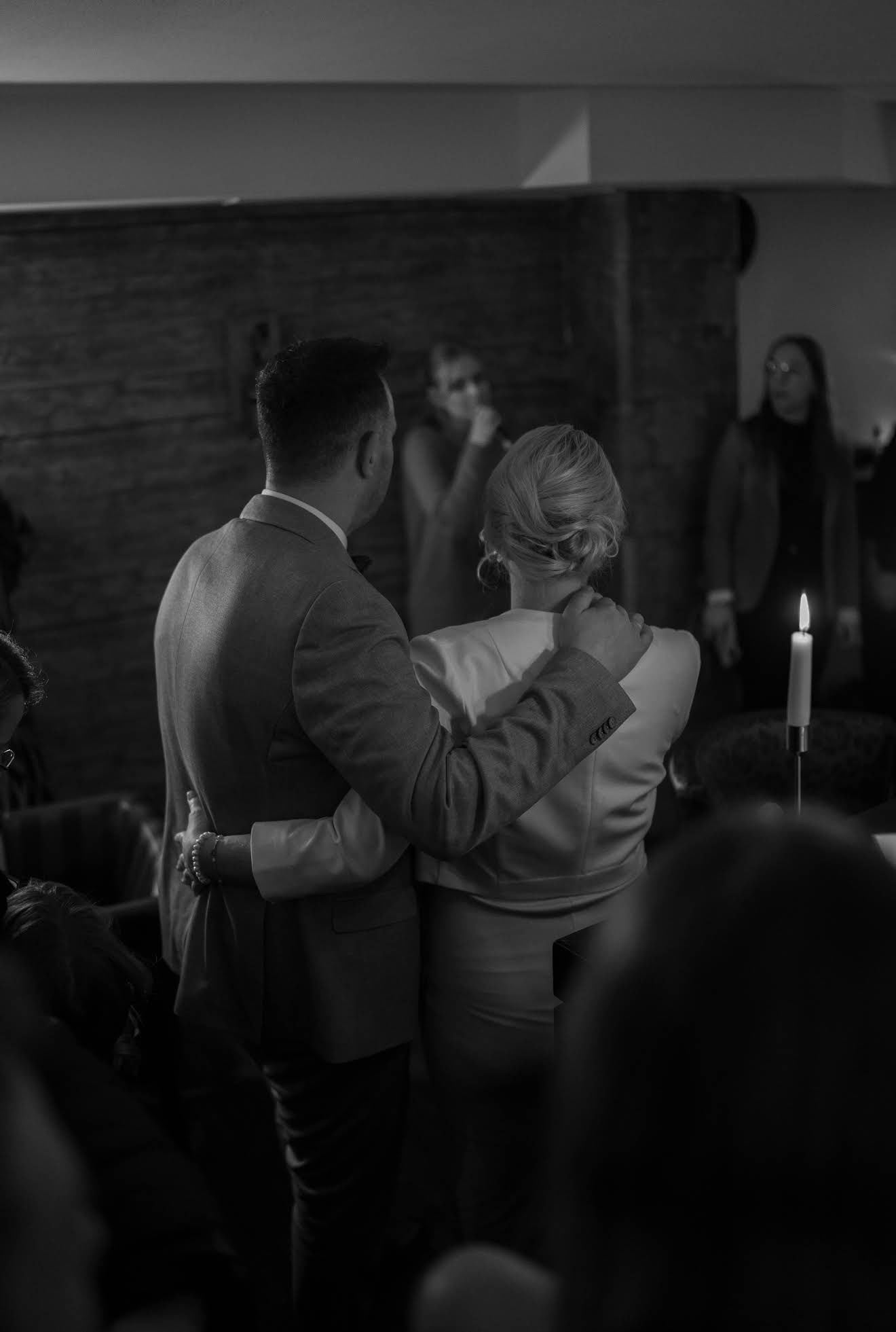 Brautpaar steht Arm in Arm und hört Hochzeitssängerin zu