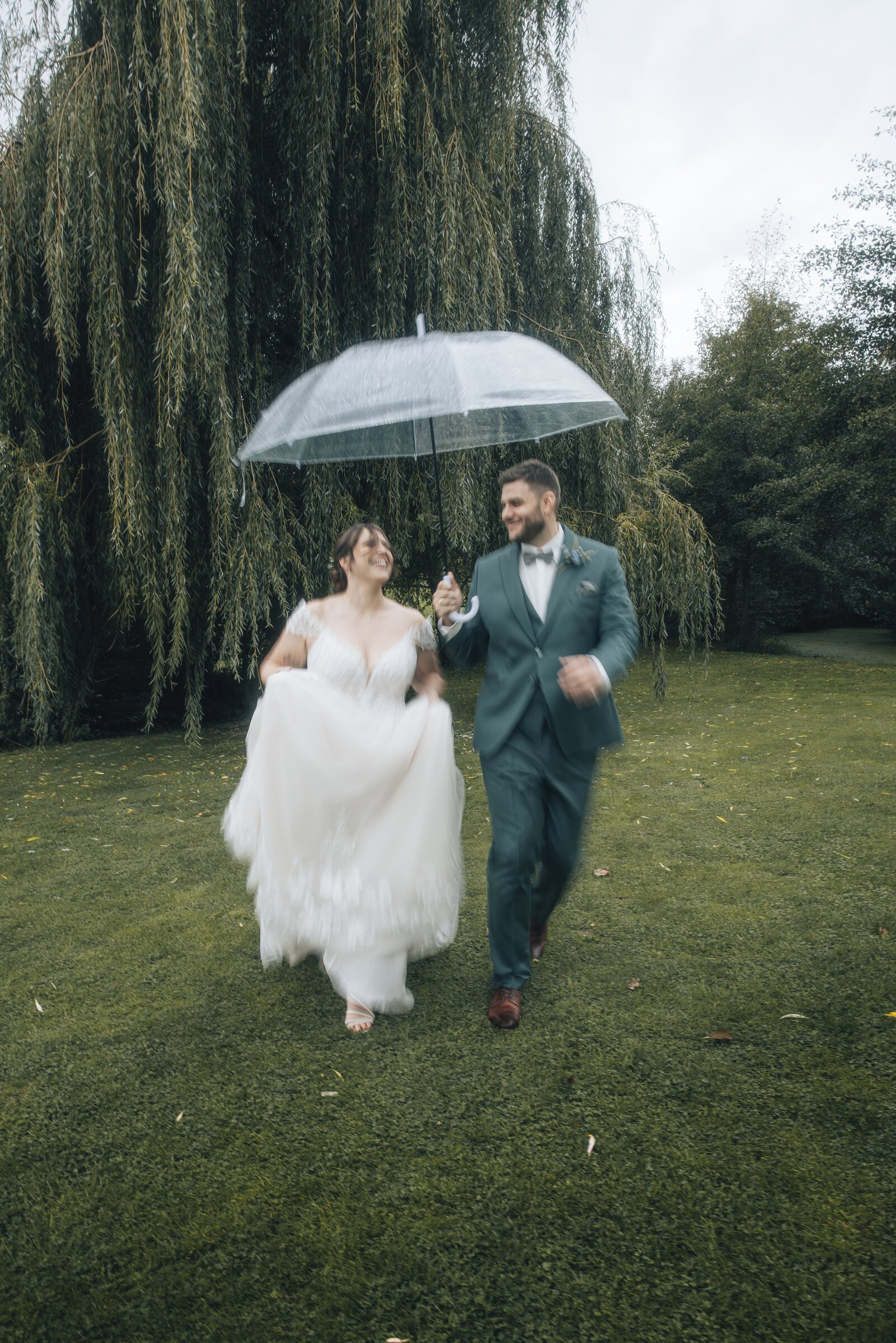 Brautpaar rennt über eine Wiese mit Regenschirm in der Hand