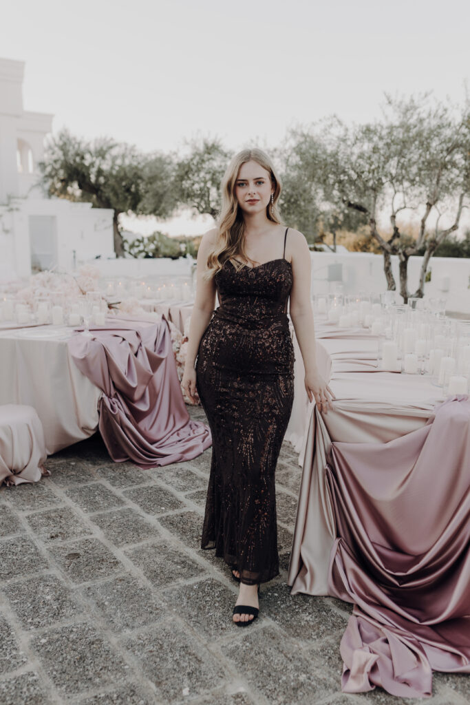 Hochzeitssängerin trägt elegantes Glitzerkleid und steht vor gedeckten Tischen.